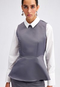 Pelēks peplum tops, satīna audums, bez piedurknēm ar baltu pogu apkakli, ar gludu tekstūru un strukturētu formu.