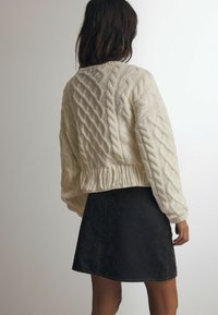 Creme kabelstrikket sweater med cropped design og frynset fald, parret med en mørk denim nederdel med en subtil tekstur og solidsnit.