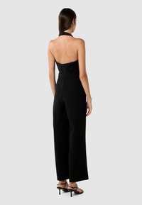 Svart ryggradsløs jumpsuit med vid buksdesign. Laget av glatt stoff, med halterneck og høyt liv. Pyntet med tynne stropper.