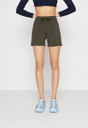 Olivgröna shorts med dragsko i midjan, med flat front och sidoseam. Matchas med ljusblå, chunky sandaler med band.