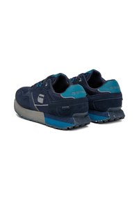 Tumši zilas sporta kurpes ar acs un zamšāda virsū, ar kontrastējošu tējas akcentu, teksturētu pelēku zoli un izteiksmīgu G-Star logotipu uz papēža.