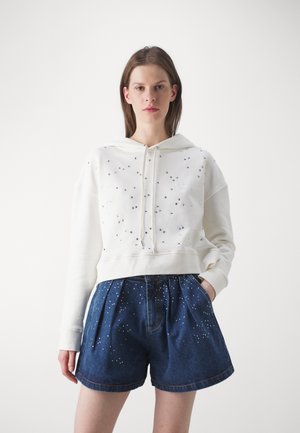 White cropped hoodie with a drawstring and scattered silver embellishments; paired with high-waisted denim shorts featuring similar decorations.
