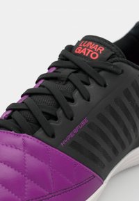 Violetas un melnas sporta kurpes ar strukturētu, kviltiem apdari, auklām un sarkanu "Lunar Gato" uzlīmi; izceļas ar "Hyperfuse" zīmolu un elegantu dizainu.