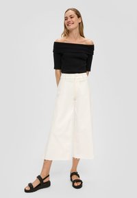 Czarna bluzka na ramiączkach, białe spodnie szerokie z postrzępionym dołem i czarne plecione sandały. Gładki materiał, minimalistyczny design.