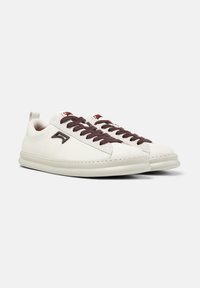 White leather low-top sneakers with dark brown laces, a black side logo, and a cream-colored sole on a light gray background.