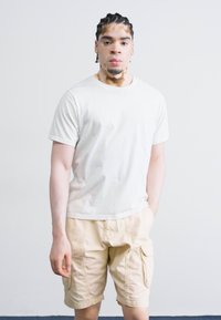 Tricou alb din bumbac și pantaloni scurți cargo bej. Pantalonii scurți au buzunare laterale și o croială lejeră. Design simplu, textură netedă și culoare deschisă.