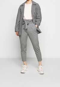 Szare krótkie spodnie z wiązanym pasem i kieszeniami bocznymi, połączone z jasnoróżową koszulką i czarno-białą marynarką w kratę. Białe sneakersy.