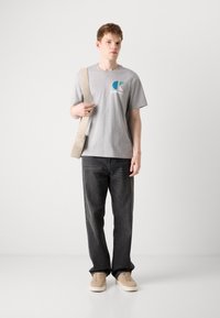 Grå bomulds t-shirt med et farvet logo, parret med mørke denim jeans og beige sneakers. En skuldertaske i neutrale farver fuldender looket.