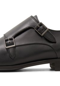 Zapato de vestir de cuero negro con acabado liso, correas de doble hebilla y un tacón bajo apilado con detalles de costura en contraste.