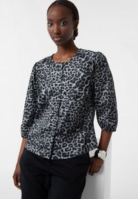 Leopardenmuster-Bluse in Grautönen, mit rundem Ausschnitt, Dreiviertelärmeln und glatter Textur. Kombiniert mit schwarzen Hosen.