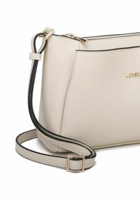 Bolso bandolera de cuero beige con ribetes negros, que cuenta con un cierre de cremallera y una correa ajustable, una sutil marca y una textura suave.