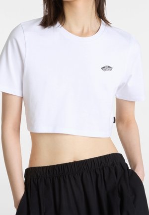 Osoba ubrana w biały crop top Vans z małym logo na klatce piersiowej i czarne spodnie z wysokim stanem, widoczna od ramion do bioder.