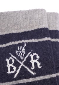 Mörkblå strumpor med grå ränder, med en vit logotyp och korsade linjer-design. Tillverkade av strukturerad stickad tyg.