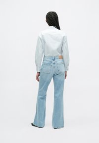 Jasnoniebieskie dzwony z wysokim stanem, z dwoma tylnymi kieszeniami i skórzaną naszywką. Połączone z koszulą w paski zapinaną na guziki.