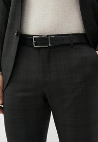 Black checkered suit pants made of a textured fabric with subtle green lines. Paired with a black leather belt featuring a silver buckle.