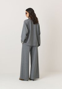 Pilkas per didelis laisvas megztinis ir plataus kirpimo kelnės švelniai tekstūroje. Išskirtiniai bruožai apima nuleistus pečius ir laisvą siluetą, derinamas su aukštakulniais.