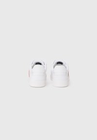 Sneakers bianchi con superficie in pelle liscia, caratterizzati da un accento rosso sul tallone, forma tondeggiante della punta e suole piatte.