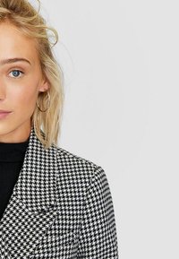 Zwart-witte houndstooth blazer met een geknipt col, twee voorzakken, textuurstof en een getailleerde pasvorm.