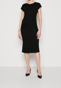 Svart, figursydd midiklänning i mjukt, stretchigt material med korta ärmar och sidsamling. Matchas med svarta högklackade skor.