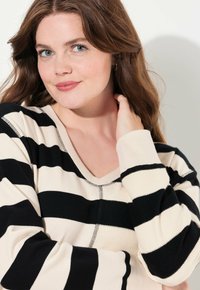 Maglione a righe in maglia con colori nero e crema, scollo a V, maniche lunghe e dettagli di cucitura visibili lungo le cuciture.