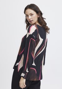 Chemise à manches longues avec des motifs abstraits noirs, roses et beiges. Fabriquée en tissu léger, elle a une coupe décontractée et des manches plissées.