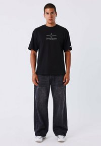 Camiseta de algodón negra con un estampado gráfico en strass, combinada con jeans de mezclilla oscuros y holgados, y zapatillas blancas.