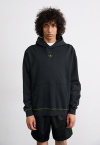 Svart hoodie med gröna detaljer, klassisk passform, känguruficka och huva. Har logotyp på bröstet och kontrasterande sömdetaljer.