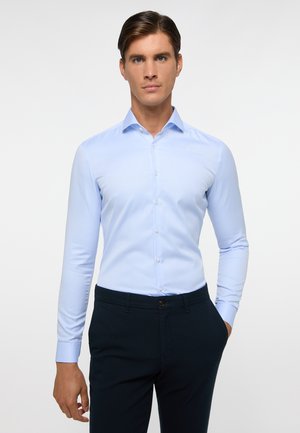 Helles blaues Hemd mit passgenauer Schnittführung, langen Ärmeln und einem Button-Down-Kragen, aus glattem Stoff gefertigt. Kombiniert mit dunklen Hosen.