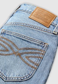 Poche arrière d’un jean en denim bleu clair avec des surpiqûres orange en motif ondulé et un patch en cuir marron de la marque Levi Strauss & Co.