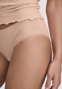 Nude stof slip met golfvormige kanten afwerking aan de benen, zachte textuur en een naadloos ontwerp, gecombineerd met een bijpassend fitted top.