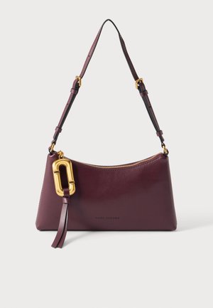 Sac à bandoulière en cuir violet foncé avec une sangle réglable, une fermeture éclair dorée et une grande boucle décorative dorée avec un pompon en cuir.