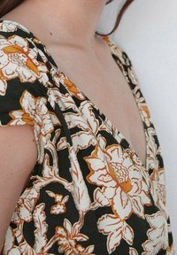 Florales Kleid mit dunkelgrünem Hintergrund und weißen sowie orangefarbenen Blumen. Das Design verfügt über einen tiefen V-Ausschnitt und kurze Ärmel.