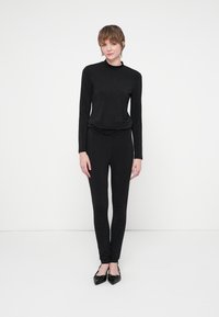 Fekete, hosszú ujjú felső és testhezálló leggings, amely texturált felülettel rendelkezik, véletlenszerűen elhelyezett ezüst pöttyökkel díszítve, kiegészítve orrhegyes lapos cipőkkel.