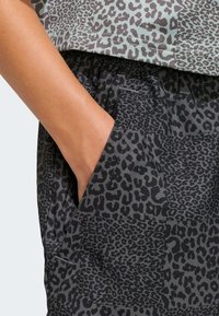 Čierna látka s leopardím vzorom, ktorá obsahuje voľný vrchný diel s krátkymi rukávmi, doplnený o šortky s elastickým pásom a bočnými vreckami.