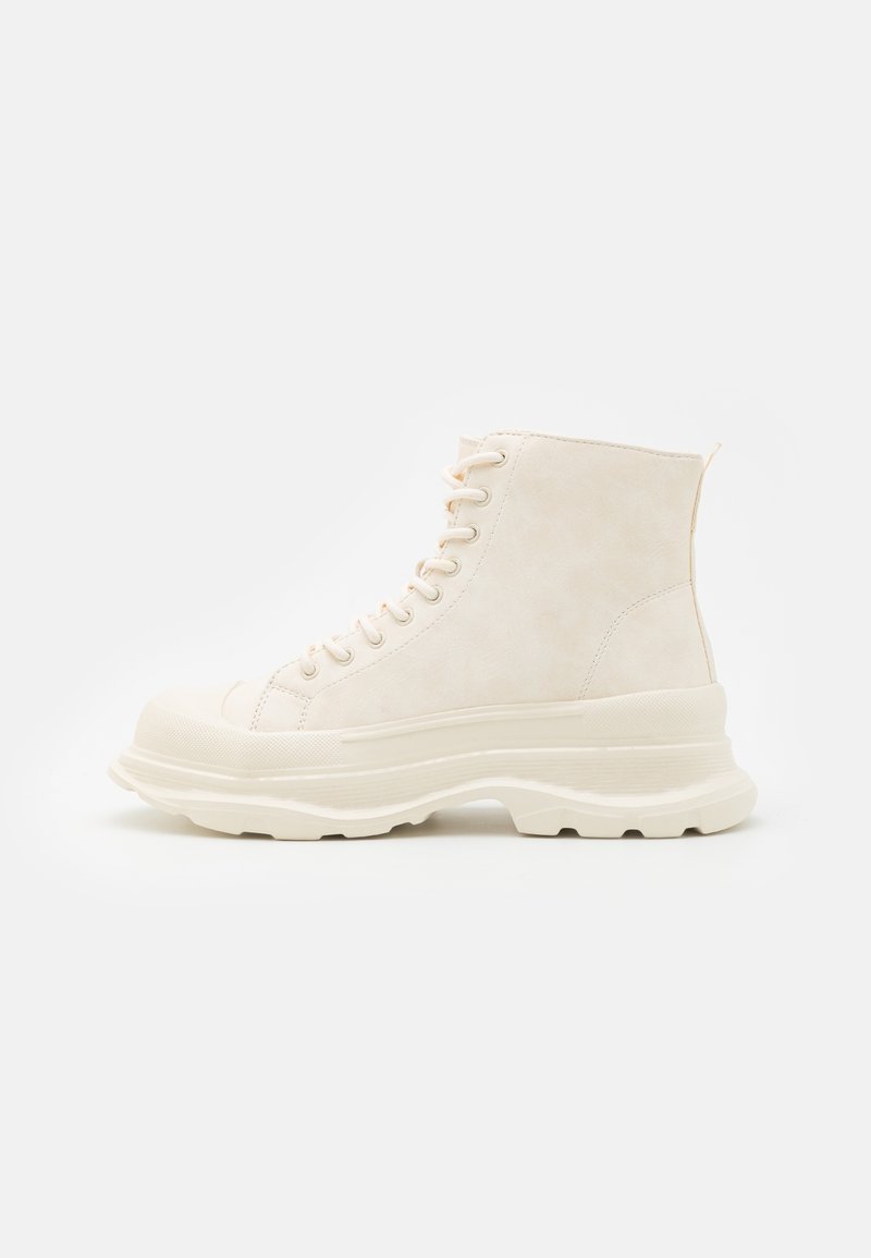 Botte basket beige montante avec semelle plateforme épaisse, bout arrondi et laçage sur un fond blanc.