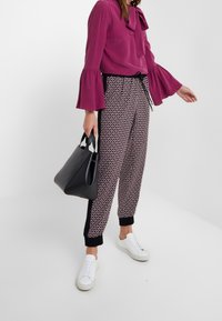 Paarse lange mouw blouse met strikdetail, gecombineerd met zwart-witte gestreepte broeken en witte sneakers. Accessoires zijn een zwarte handtas.