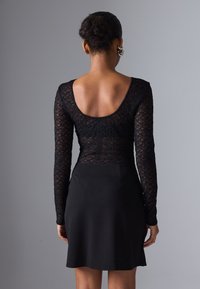 Top din dantelă neagră cu mâneci lungi și decolteu în formă de cerc, asociat cu o fustă neagră evazată. Dantela are un model complex și o textură moale.