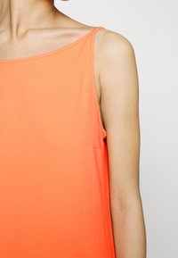 Oranžový bezrukávový top z lehkého materiálu, s rovnou výstřihovou linií a jednoduchým designem se boční kapsou. Hladká textura.