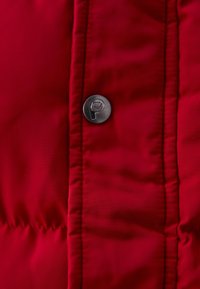 Tissu matelassé rouge avec une couture verticale et un bouton métallique rond présentant un logo d'ours en relief.