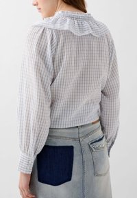 Camicia a righe azzurro chiaro e bianco con colletto arricciato e maniche lunghe a palloncino, abbinata a una gonna di jeans con una tasca scura a contrasto.