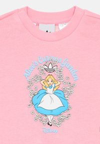 Ροζ βαμβακερό φούτερ με γραφικό της Άλις περιτριγυρισμένη από μαργαρίτες, με το κείμενο "Το Αινιγματικό Κήπο της Άλις" και λογότυπο Adidas.