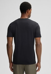 Zwarte katoenen t-shirt gezien vanaf de achterkant. Korte mouwen, ronde hals, gladde textuur en minimale stikdetails. Casual pasvorm.