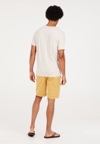 Camisa de manga corta beige y pantalones cortos amarillos, hechos de materiales ligeros. La camiseta tiene cuello redondo, los pantalones cortos cuentan con bolsillos laterales y un ajuste relajado.