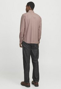 Camisa de manga larga y cuello abotonado en rosa suave, combinada con jeans de mezclilla oscuros. La camisa tiene un collar estándar y puños ajustables.