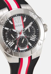 Stainless steel watch with a black dial, red and white striped silicone band, luminous hour markers, and three sub-dials.