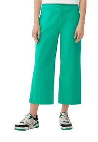 Grüne, weit geschnittene, knöchellange Hosen aus leichtem Material, mit einem Knopfverschluss und zwei seitlichen Taschen, kombiniert mit Schwarz-Weiß-Sneakern.