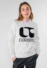 Sudadera blanca con un gran logo negro que dice "LT cerises" en la parte frontal, combinada con un cuello a rayas rosa y blanco visible abajo.