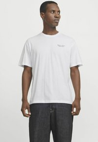 Hvid bomulds T-shirt med rund halsudskæring og korte ærmer, prydet med diskret tekst foran. Bæret med mørke denimjeans.