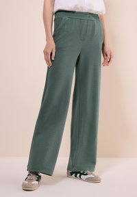 Groene, gestructureerde wijde broek met een elastische tailleband, voorzien van zijzakken en een losse pasvorm, gecombineerd met casual sneakers.