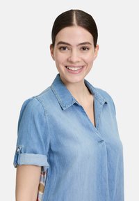 Jasnoniebieska koszula dżinsowa z krótkimi, zwijanymi rękawami, kołnierzykiem i detalem na guziku. Posiada gładką teksturę i swobodny design, odpowiednia na co dzień.